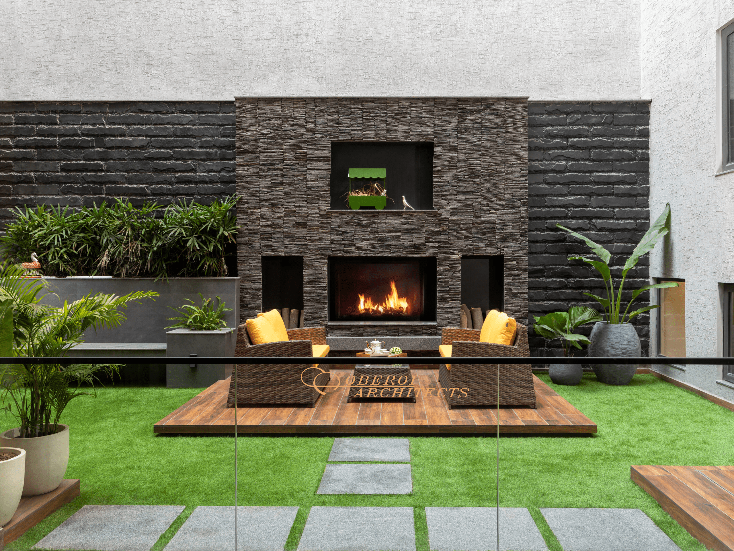Outdoor patio with fireplace, wicker chairs, artificial turf, and textured stone walls