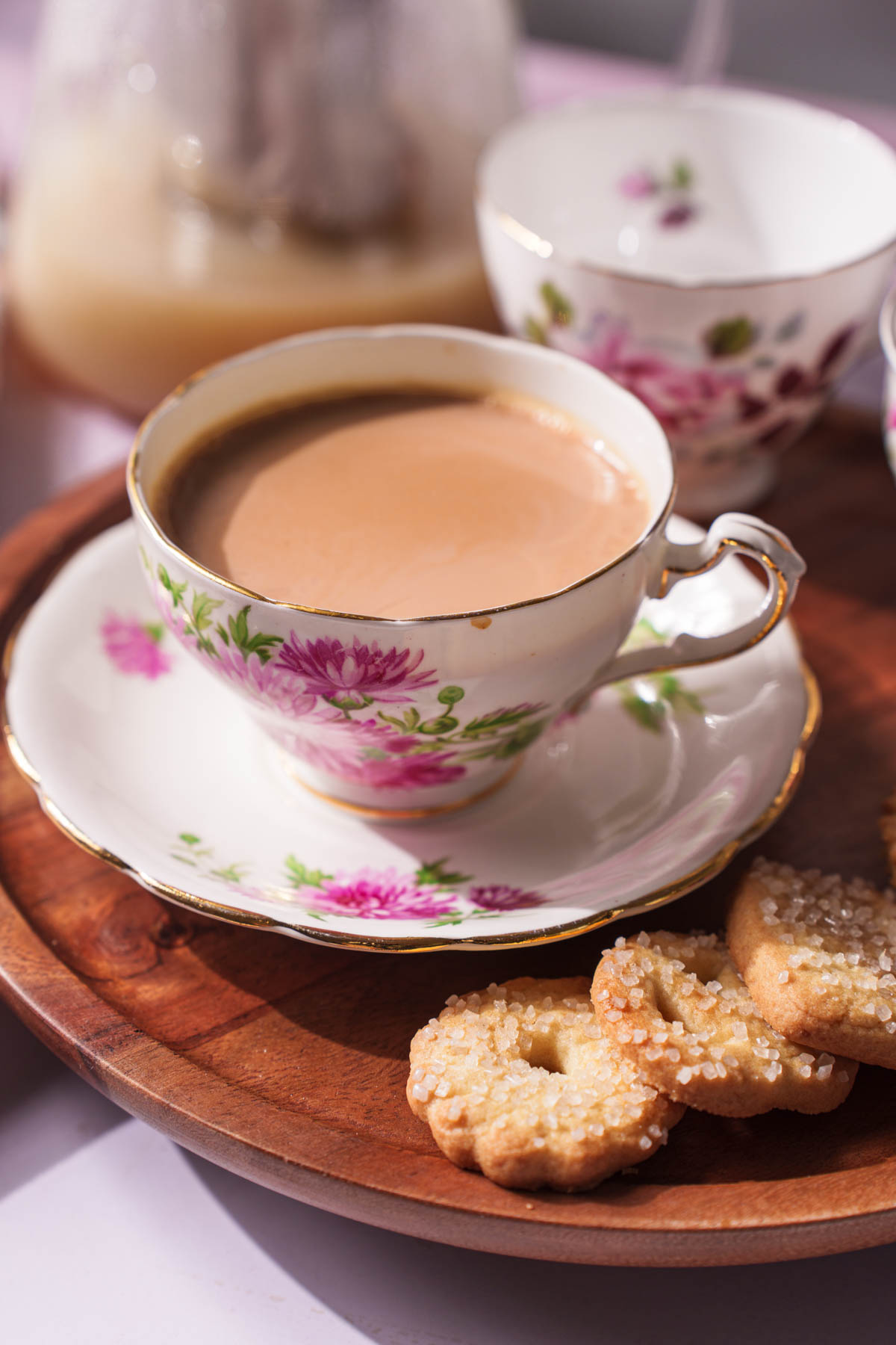 Vintage floral teacup filled with chai beside golden cookies on a wooden tray