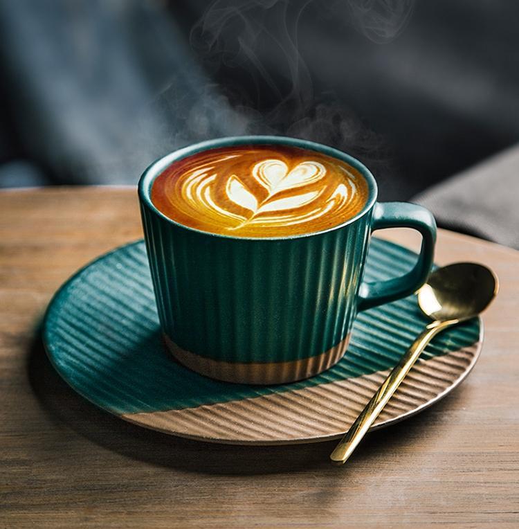 Dark green coffee cup with heart latte art on a saucer with gold spoon