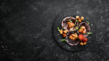 Pan-seared scallops with tomatoes and microgreens on a black plate