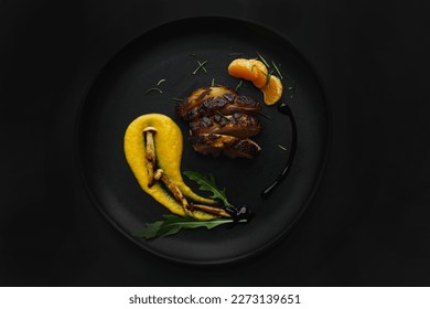 Modern gourmet plate with sliced meat, yellow puree, mushrooms, and orange segments on a dark background